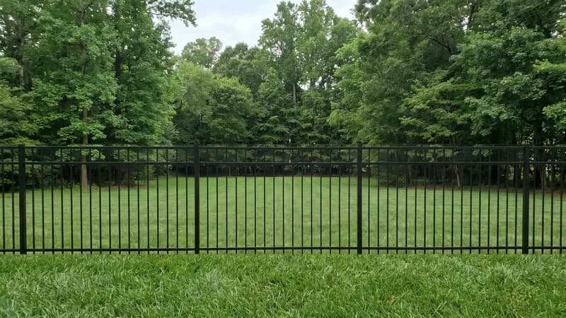 Black ornamental aluminum fence with vertical pickets along a landscaped front yard