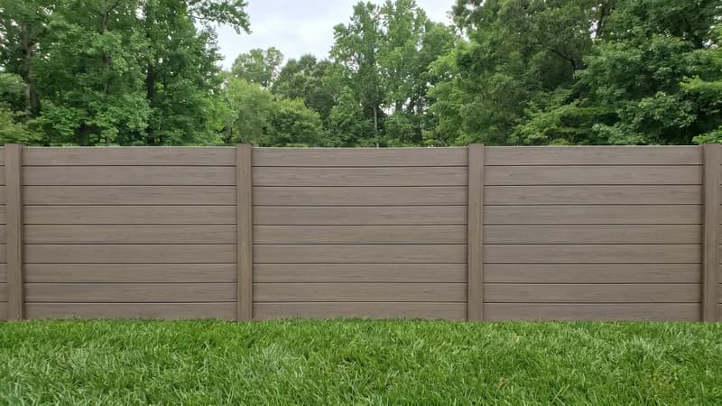 Capped composite privacy fence with horizontal taupe woodgrain boards along a mown lawn