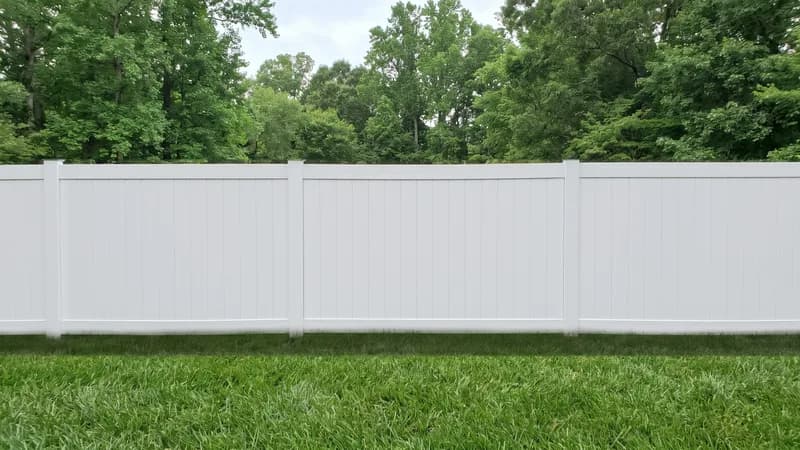 White vinyl privacy fence panels along a manicured suburban backyard under a blue sky